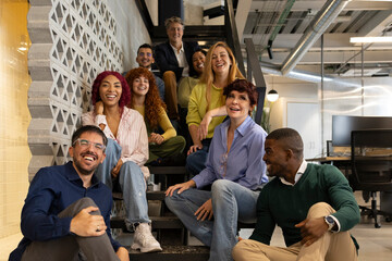 Coworkers smiling and sitting on stairs in modern office