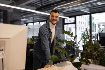 Young businessman smiling in modern coworking office with plants and computers