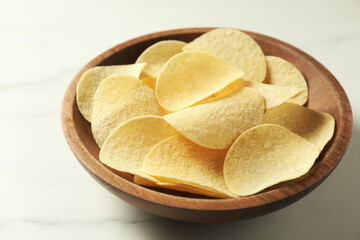 Tasty potato chips in bowl on white marble table, closeup