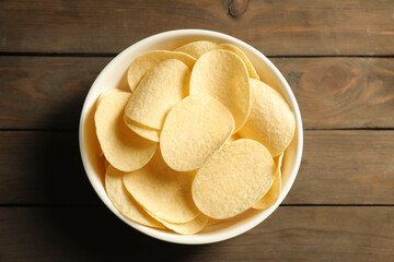 Tasty potato chips in bowl on wooden table, top view