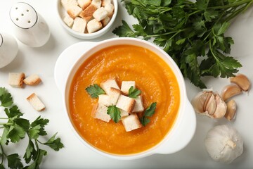 Tasty pumpkin cream soup with croutons, parsley garlic and spices on white table, flat lay