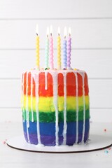 Delicious rainbow birthday cake with burning candles and sprinkles on white table