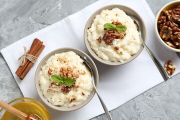 Delicious rice pudding with walnuts, cinnamon, mint and honey on grey table, flat lay