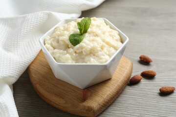 Delicious rice pudding in bowl, almonds and mint on wooden table, closeup
