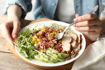 Woman eating delicious salad with brown rice at wooden table, closeup