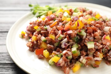 Tasty salad with brown rice on black wooden table, closeup
