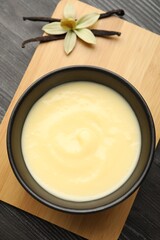 Tasty vanilla pudding in bowl, flower and pods on wooden table, top view