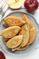 Delicious fried pyrizhky (stuffed pies) and apples on white wooden table, flat lay