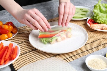 Woman making tasty spring roll at light grey table, closeup