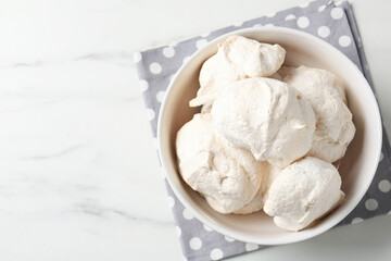 Delicious homemade meringue cookies in bowl on light marble table, top view. Space for text