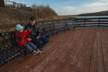 Fototapeta premium Father and daughter sitting in the bench at the pier near the lake.