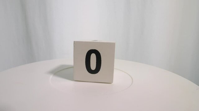 Wooden cube with the numbers 0,8,6, and 2 on a turntable on a white background. Slow motion.