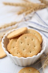 Tasty salty crackers with wheat spikes on white table, closeup