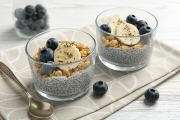 Delicious dessert with chia seeds, yogurt, granola, blueberries and banana on white wooden table, closeup. Superfood