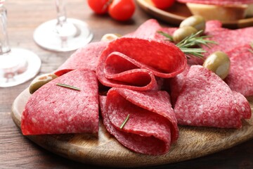 Slices of delicious sausage with olives and rosemary served on wooden table, closeup