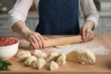 Making khinkali. Woman with rolling pin shaping piece of dough at table in kitchen, closeup