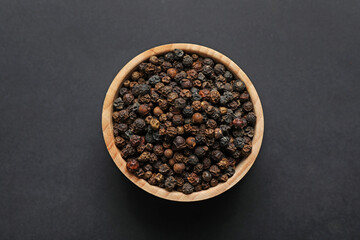 Aromatic peppercorns in bowl on dark table, top view
