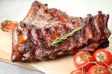 Tasty roasted pork ribs served with rosemary, tomatoes and sauce on light grey table, closeup
