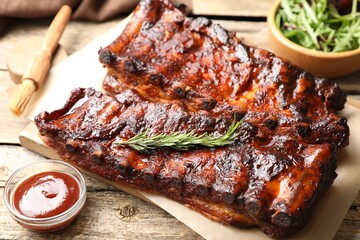 Tasty roasted pork ribs served with rosemary, sauce and salad on wooden table, closeup