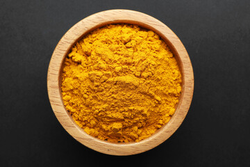Turmeric powder in bowl on black background, top view. Aromatic spice