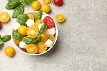 Fresh salad with yellow tomatoes, basil and mozzarella cheese on grey table, flat lay. Space for text