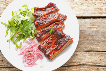 Delicious pork ribs, arugula and onion on wooden table, top view