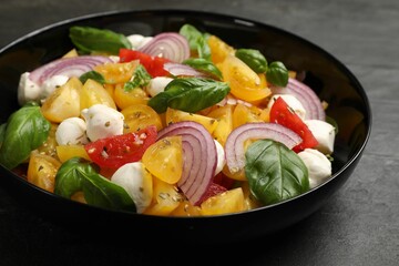 Tasty salad with yellow tomatoes, basil, onion and mozzarella cheese on black table, closeup