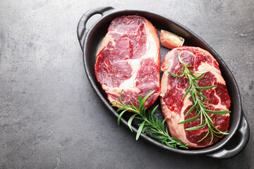 Pieces of raw beef meat and spices in baking dish on gray textured table, top view. Space for text