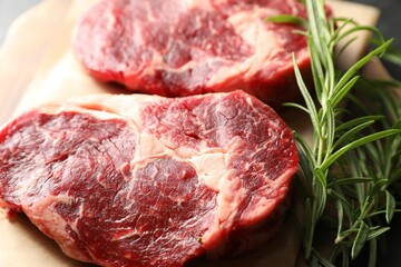 Pieces of raw beef meat and rosemary on table, closeup