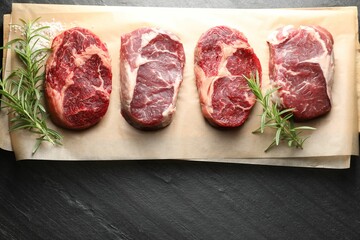 Pieces of raw beef meat, rosemary and salt on black table, top view