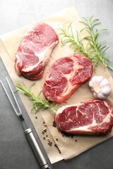 Pieces of raw beef meat, spices and carving fork on grey table, flat lay
