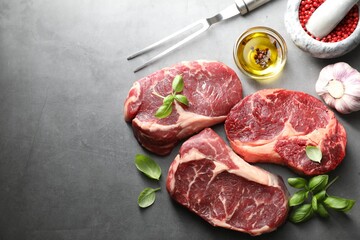 Pieces of raw beef meat, spices and carving fork on grey table, flat lay. Space for text