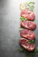 Pieces of raw beef meat and spices on grey table, flat lay. Space for text