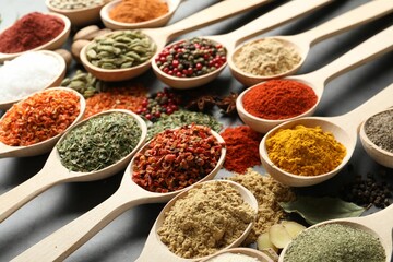 Many different spices in spoons on grey table, closeup