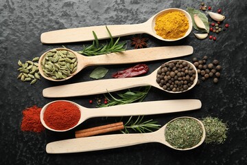 Many different spices in spoons on black table, flat lay