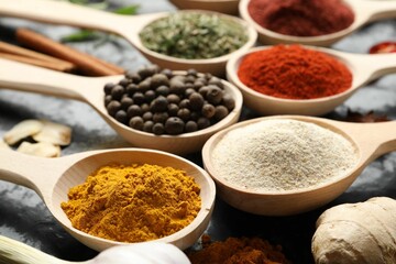 Many different spices in spoons on black table, closeup