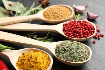 Different aromatic spices in spoons on black table, closeup