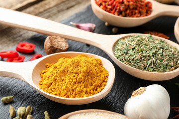 Different aromatic spices in spoons on wooden table, closeup