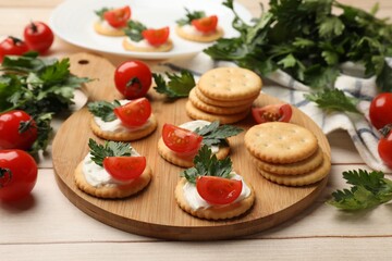 Tasty crackers with cream cheese, tomatoes and parsley on white wooden table, closeup