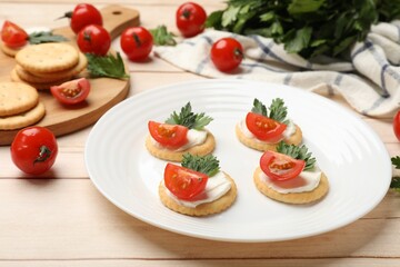 Tasty crackers with cream cheese, tomatoes and parsley on white wooden table, closeup