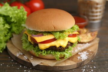 Tasty cheeseburger with potato wedges on wooden table, closeup