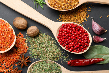 Different aromatic spices in spoons on black table, flat lay