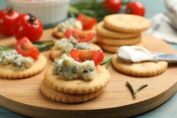 Tasty crackers with blue cheese, rosemary and tomatoes on wooden table, closeup