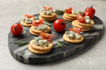 Tasty crackers with blue cheese, rosemary and tomatoes on grey textured table, closeup