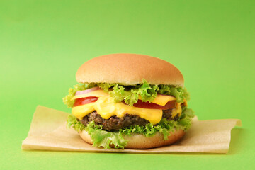 Tasty cheeseburger with sauce on green background, closeup