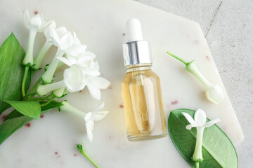 Bottle of essential oil and jasmine flowers on light grey table, top view