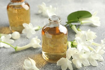Bottles of essential oil and jasmine flowers on grey table, closeup