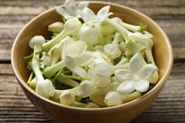 Beautiful jasmine flowers in bowl on wooden table, closeup