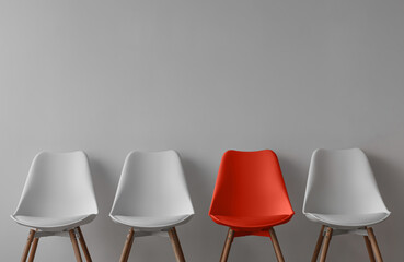 Three white chairs and red on gray wall background in office or room. Row of stools with one of...