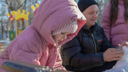 Grandfather with granddaughters making a little snowman in sunny winter day